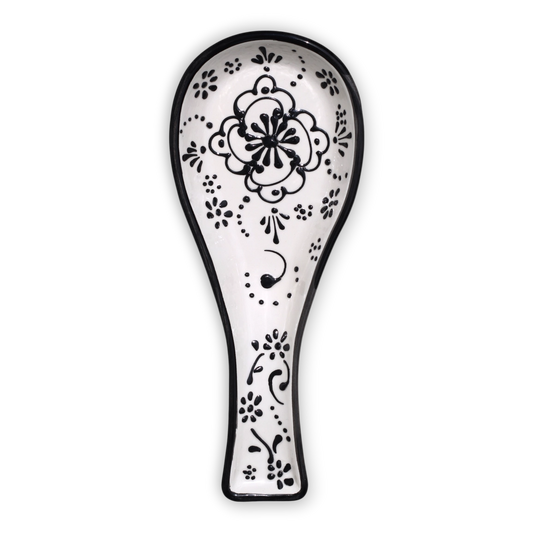 A white ceramic spoon rest with a black hand-painted floral and scroll pattern, shown against a plain white background.