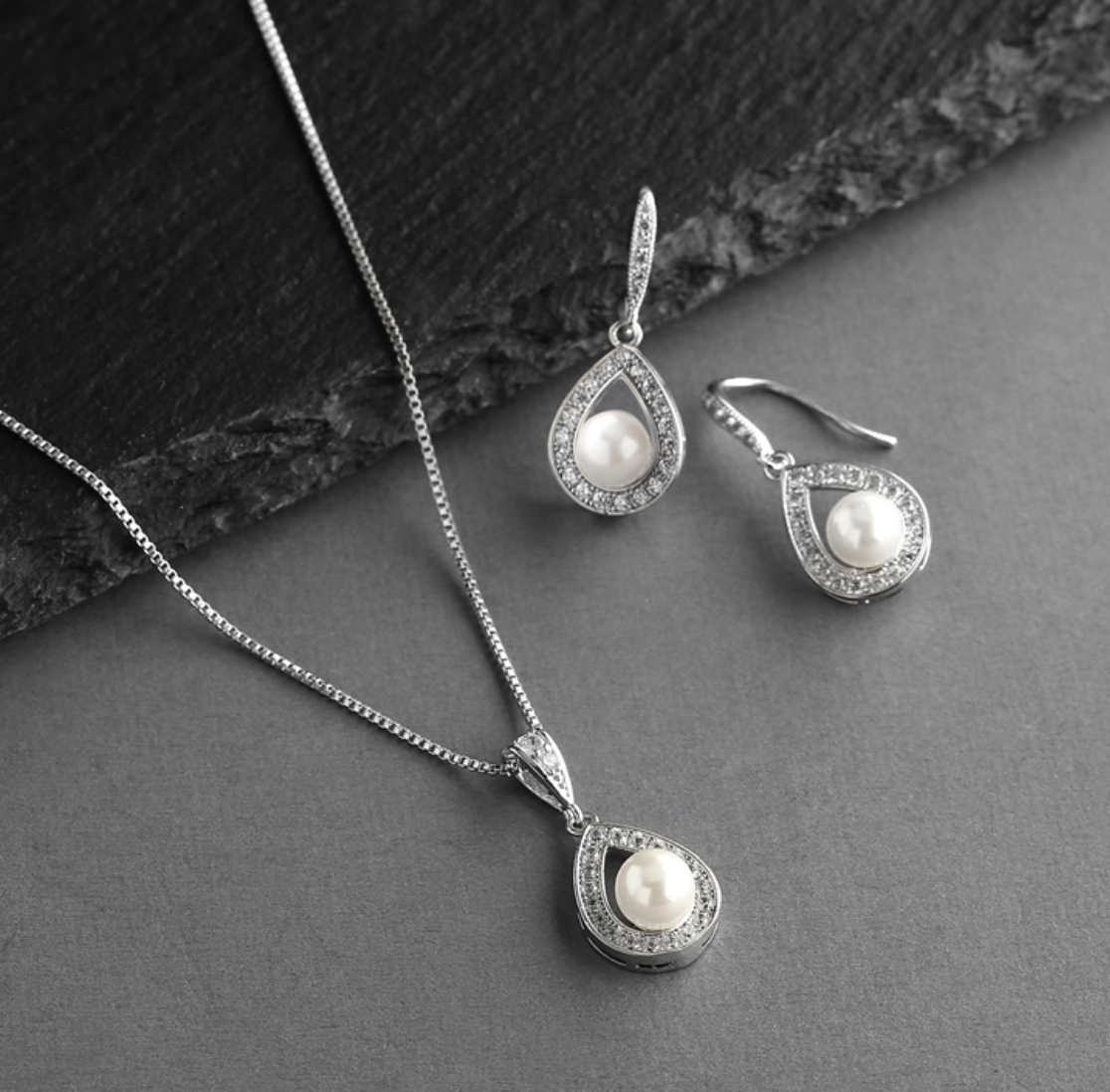 Silver jewelry set with pearl accents on a dark surface