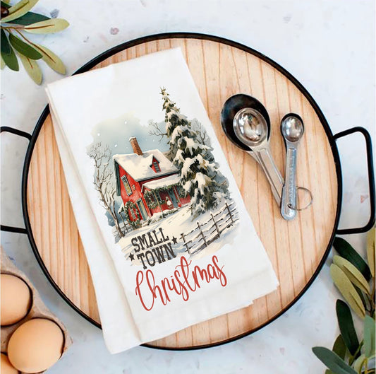 Tea towel with 'Small Town Christmas' design on a wooden board with measuring spoons and eggs.