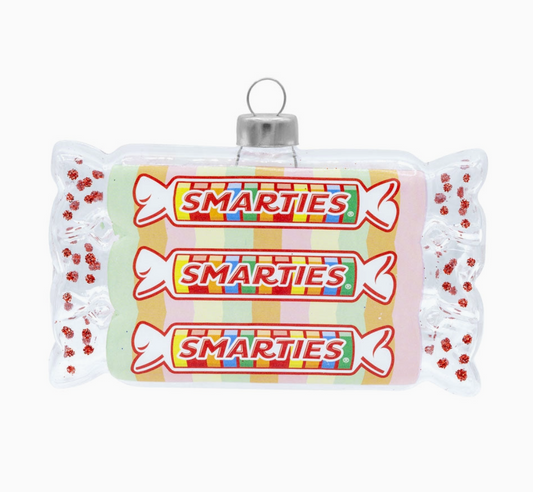 A novelty Christmas ornament shaped like a Smarties candy bar wrapper, featuring three printed Smarties logos and colorful striped details, with a silver hanging loop at the top.