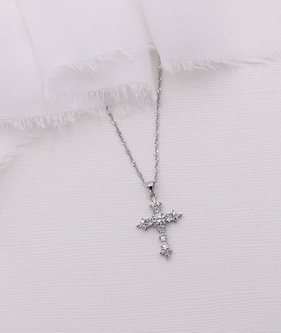 Silver cross necklace with clear stones on a white textured fabric background