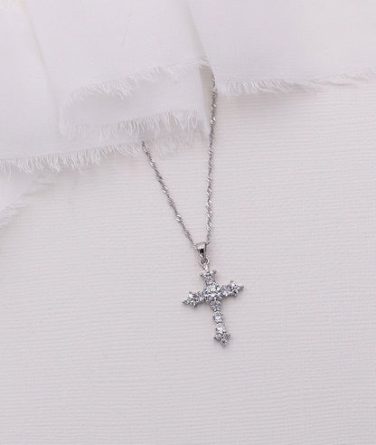 Silver cross necklace with clear stones on a white textured fabric background