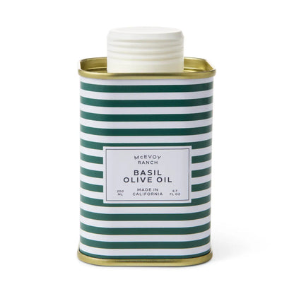 A 220 mL metal can of McEvoy Ranch Basil Olive Oil, featuring a white screw cap and a green and white striped body with gold metal rims, set against a plain white background.