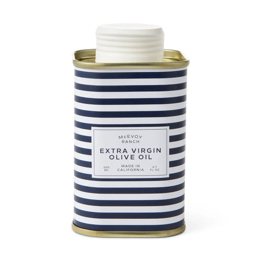 A cylindrical metal can of McEvoy Ranch Extra Virgin Olive Oil with a navy blue and white striped pattern, a white screw cap, and gold-colored rims at the top and bottom.