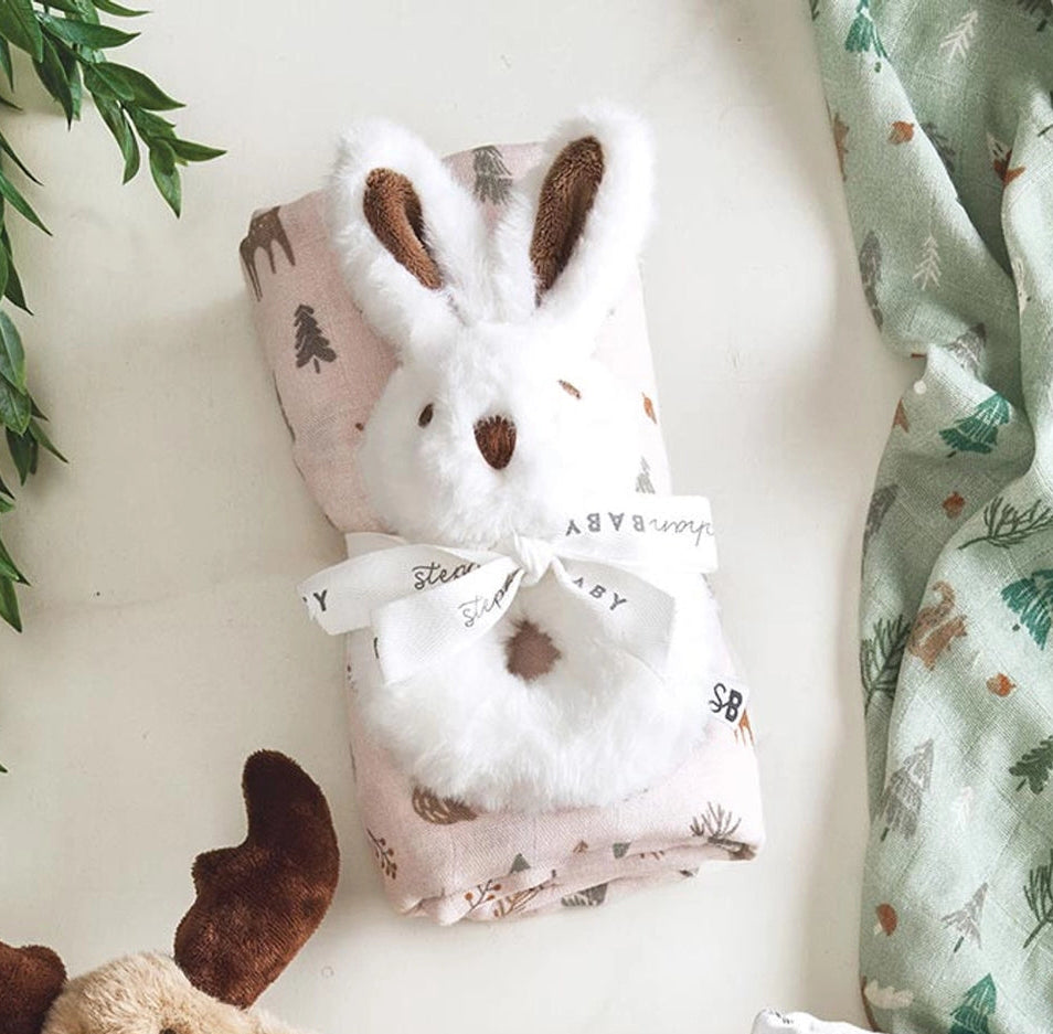 Baby swaddle with animal pattern, plush toy, and green fabric on a light background