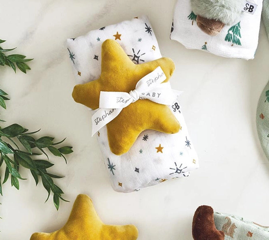 Two yellow star-shaped toys and a plush moose toy on a white surface with greenery.