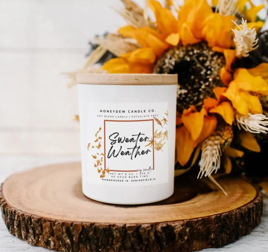 Candle labeled 'Sunflower Weather' on a wooden coaster with sunflowers and pinecones.