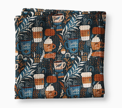 Sweater Weather fall waffle weave kitchen towel with coffee mugs, pumpkins, autumn leaves and acorns on a dark navy background.