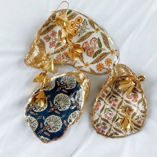 Decorative oyster shell trinket dishes with floral and gold patterns on a white background
