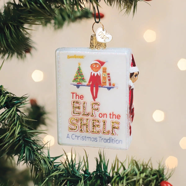 Decorative ornament with 'Elf on the Shelf' design hanging on a Christmas tree.
