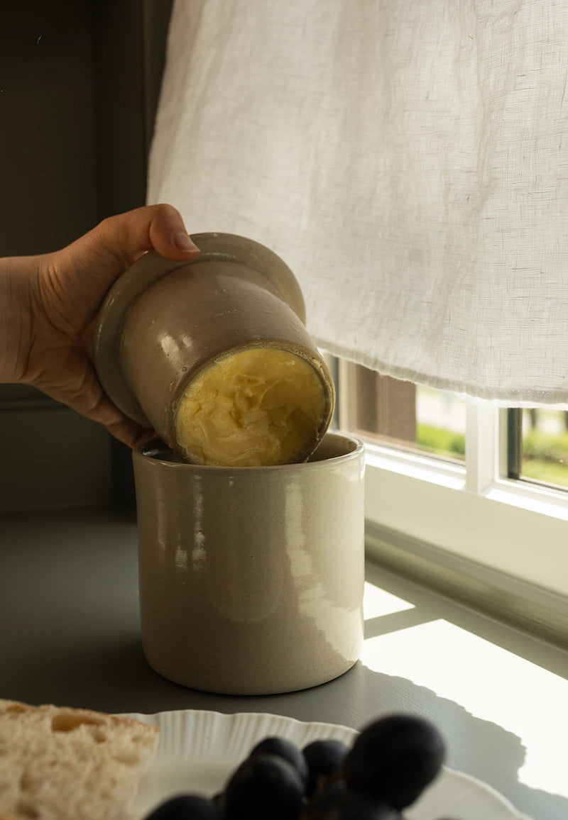 Person showing butter in a butter keeper ceramic container on a windowsill.