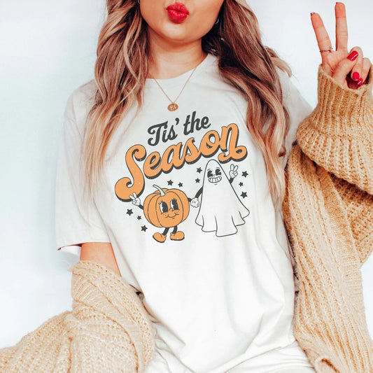 Person wearing a white t-shirt with Halloween-themed design, including a ghost and pumpkin, against a plain background.