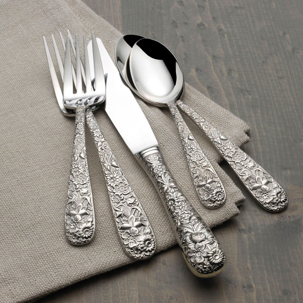 Silver cutlery set with ornate designs on a gray napkin and wooden surface