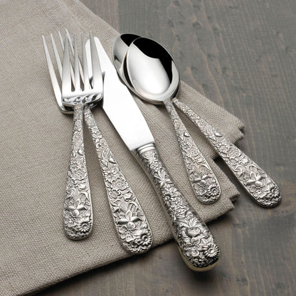 Silver cutlery set with ornate designs on a gray napkin and wooden surface