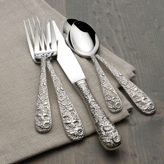 Silver cutlery set with ornate designs on a gray napkin and wooden surface