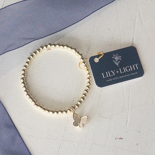 Gold bracelet with a butterfly charm on a white surface with a 'Lily + Light' tag.