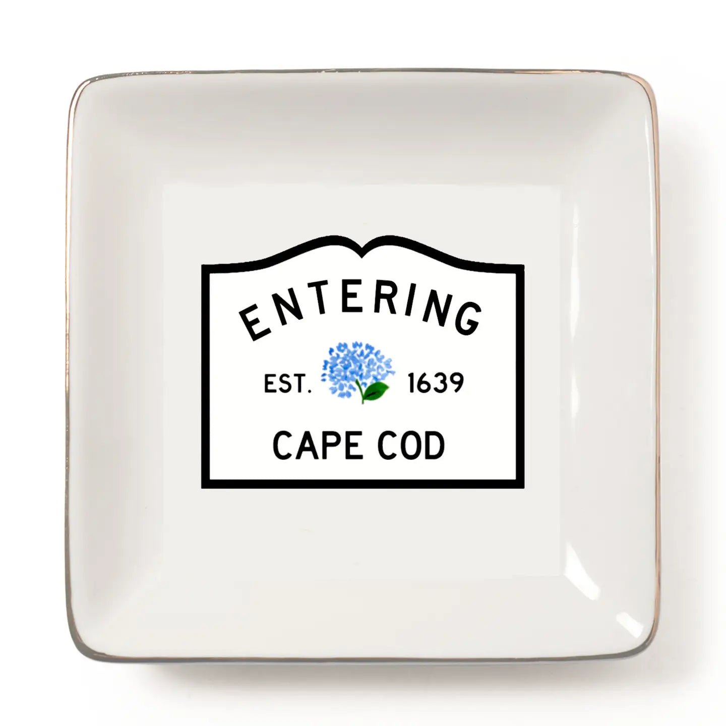 A square white ceramic dish with rounded corners and a metallic gold-toned rim, featuring a printed black-bordered label in the center that reads 'ENTERING CAPE COD EST. 1639' with a small blue flower graphic.