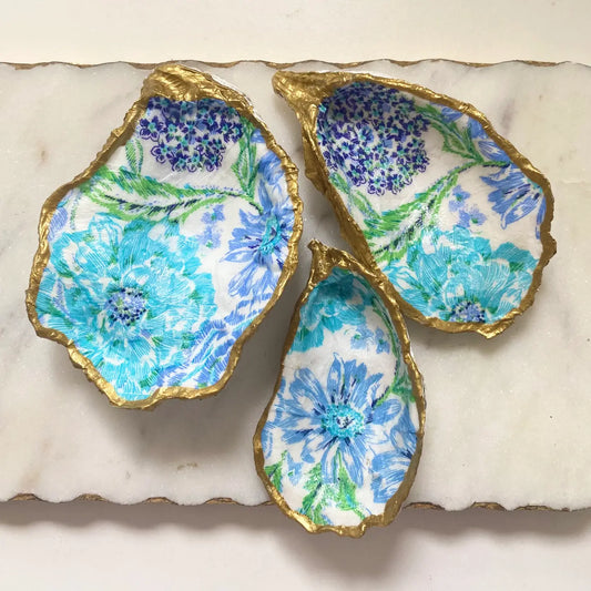 Three decorative oyster shells with floral patterns on a marble surface