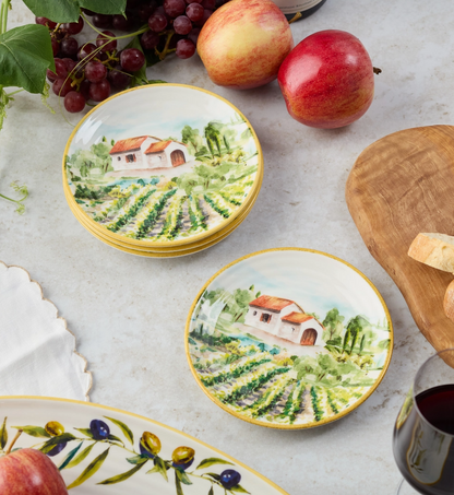 Decorative plates with vineyard design on a table with apples and grapes.