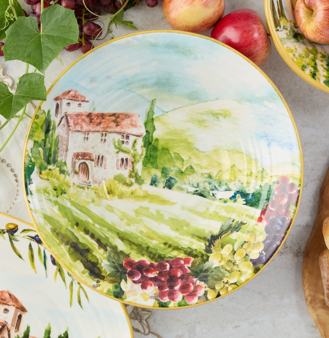 Decorative plate with a scenic design of a village and landscape, surrounded by apples and grapes.