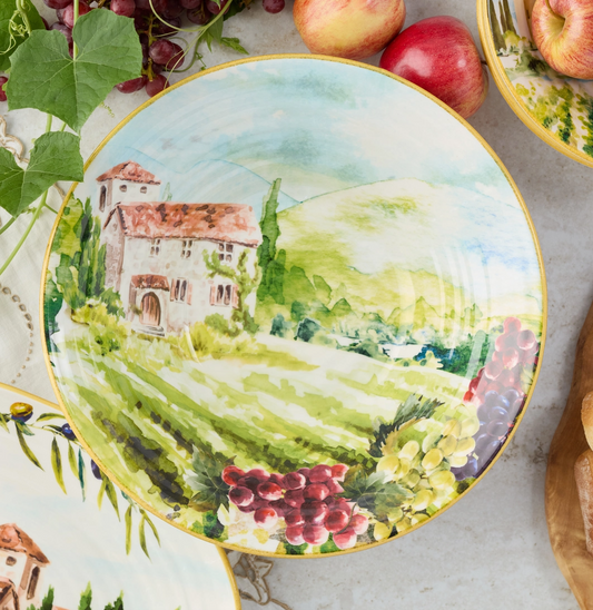 Decorative plate with a scenic design of a village and landscape, surrounded by apples and grapes.