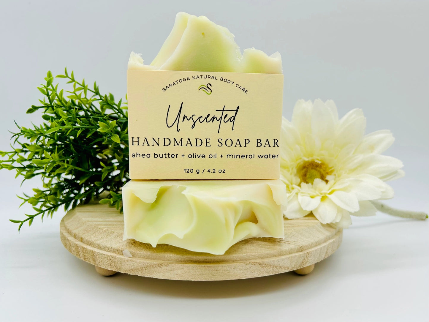 Unscented handmade soap bar on a wooden stand with a flower and greenery on a light background