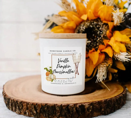 Candle with a label on a wooden surface with flowers in the background