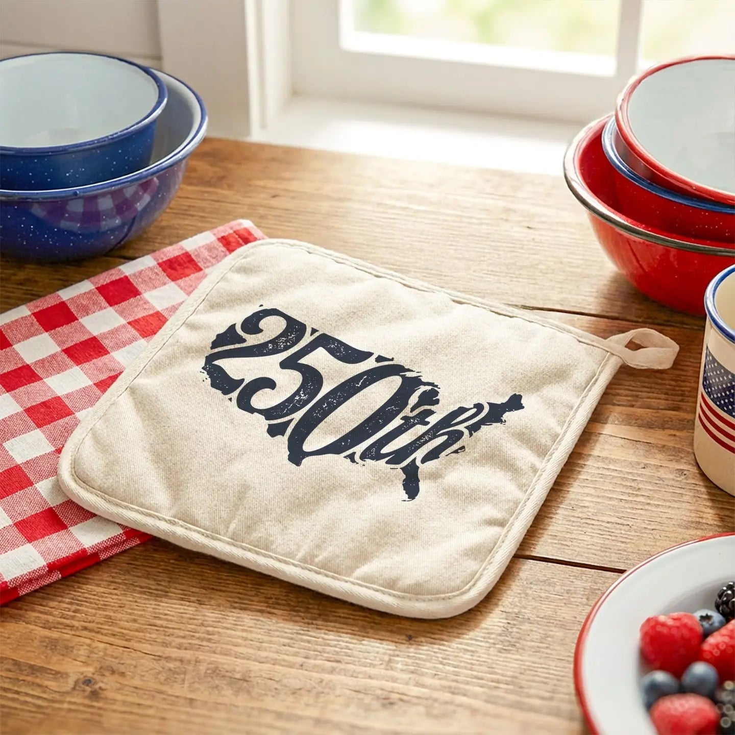 Potholder with '250th' design on a wooden table with kitchen items.