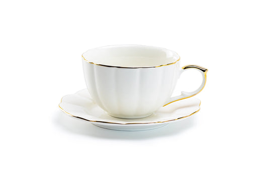 White teacup with gold trim on a white saucer against a white background