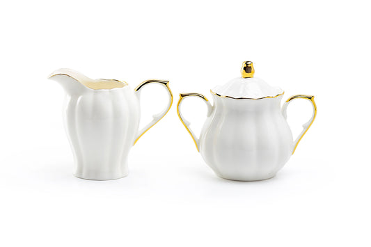 White ceramic creamer and sugar bowl set with gold accents on a white background