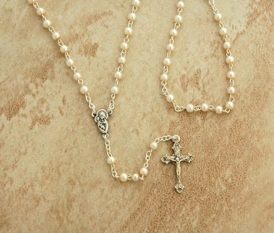 Pearl rosary necklace with a cross on a beige textured background