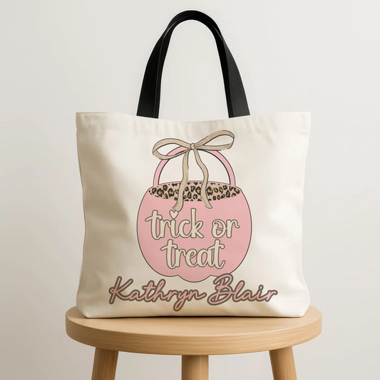 Tote bag with 'trick or treat' design and embroidered name on a wooden stool.