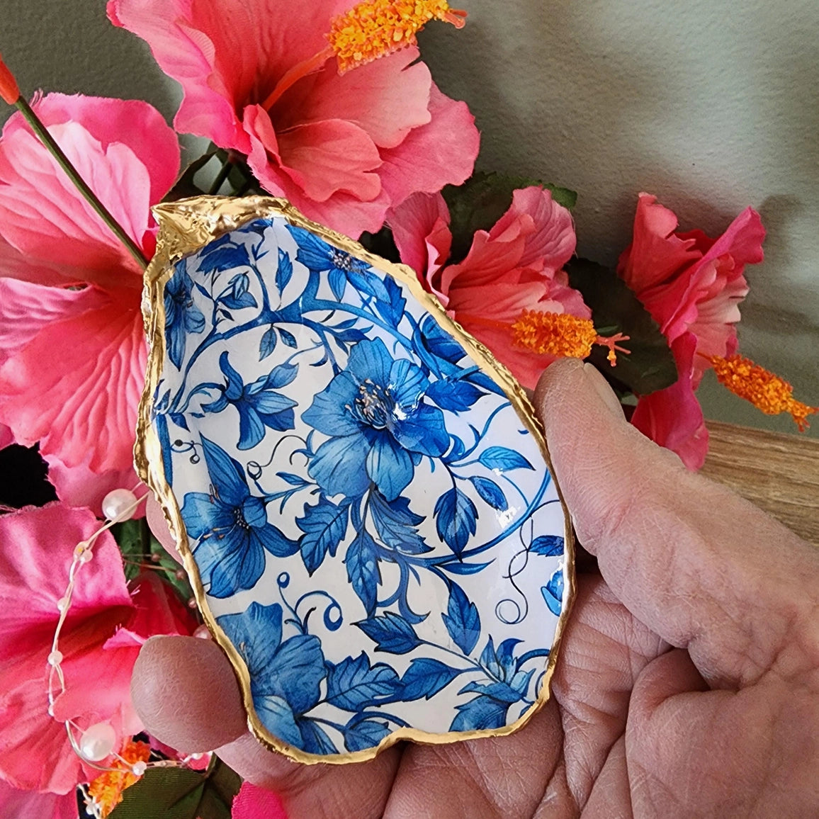 Decorative stone with blue floral pattern held among pink flowers