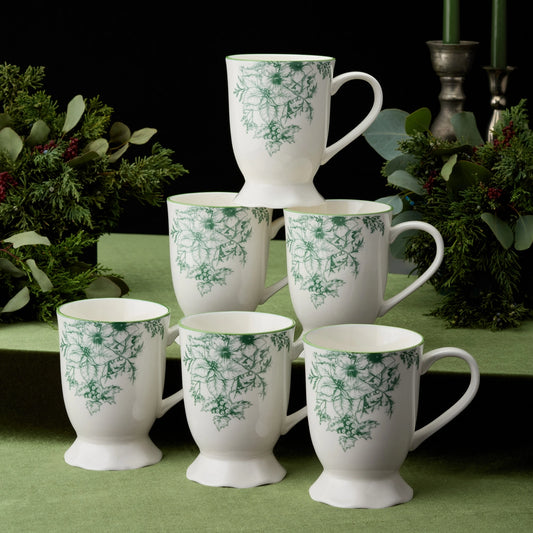 Set of white mugs with green floral patterns arranged in a pyramid on a green surface.