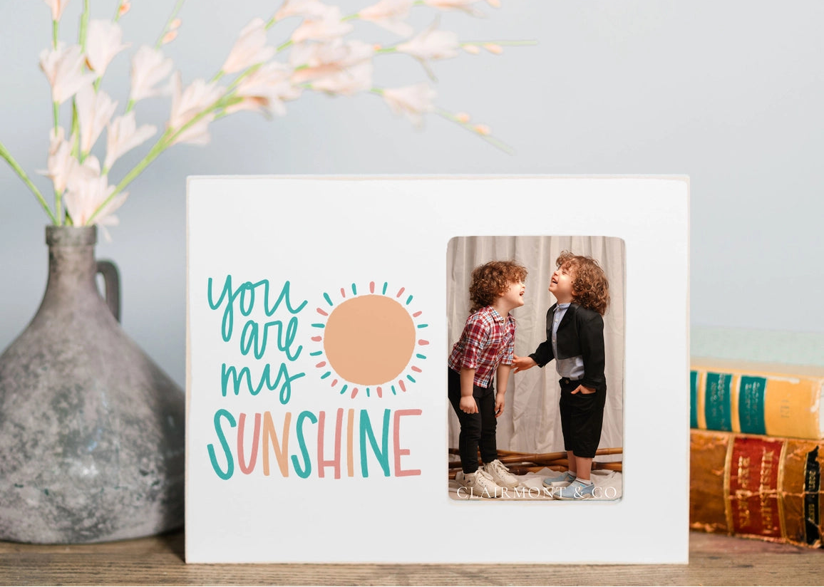 Framed photo with 'You are my sunshine' text next to a vase with flowers on a table.