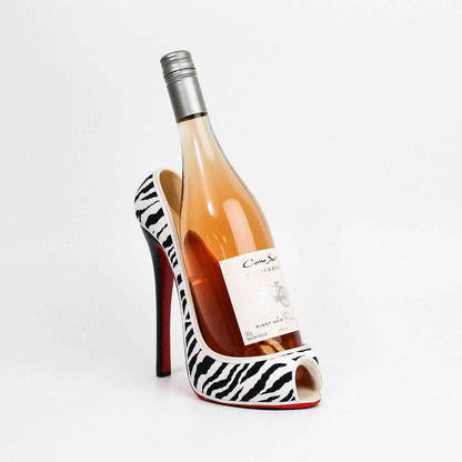 A wine bottle shaped like a high-heeled shoe, filled with rosé ginebrand wine. The heel and toe sections are white with black zebra stripes, and the sole has a signature red accent.
