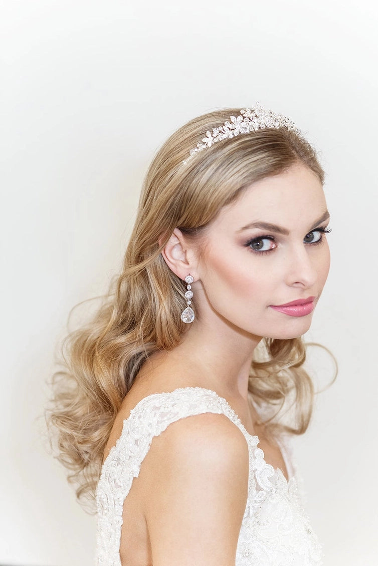 Woman wearing a tiara and earrings with a white lace top against a light background
