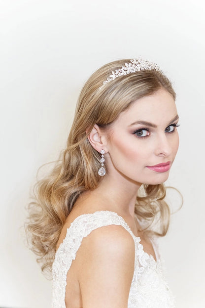 Woman wearing a tiara and earrings with a white lace top against a light background