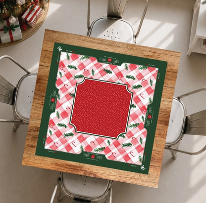 Candy Cane Lane Christmas Mahjong mat displayed on a holiday game table with pink gingham, red center and evergreen border.