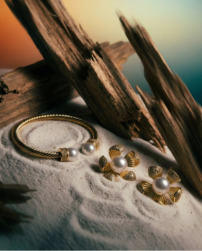 Gold jewelry with pearls on sand and driftwood against a sunset sky