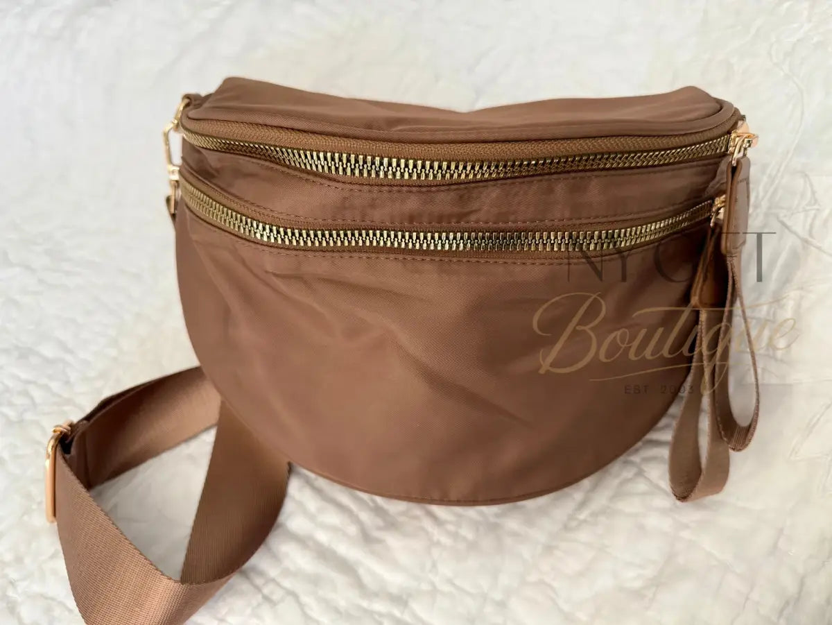 Brown fanny pack with gold zippers on a textured white background