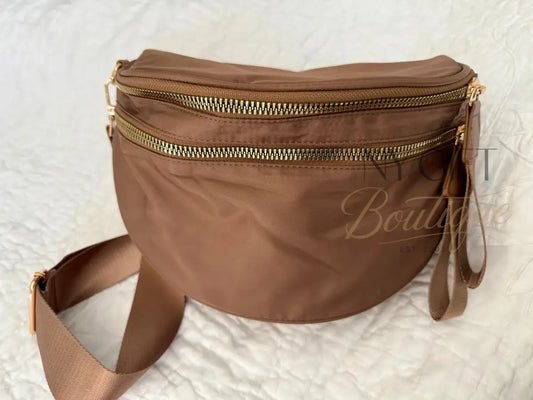 Brown fanny pack with gold zippers on a textured white background