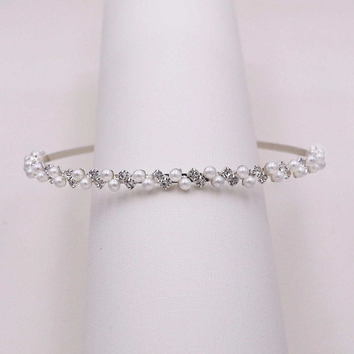 Pearl and crystal headband on a jewelry rack against a white background