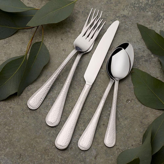 Silver cutlery set with a knife, fork, and spoons on a stone surface with green leaves.
