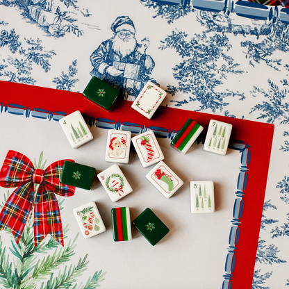 Christmas Mahjong tiles displayed on Tartan Toile Noël mat featuring red tartan bow, blue-and-white toile and holiday greenery.